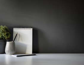 A clean and modern office workspace featuring a pen holder, notebook, and ceramic vase against a