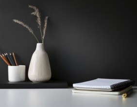 A clean and modern office workspace featuring a pen holder, notebook, and ceramic vase against a
