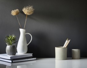 A clean and modern office workspace featuring a pen holder, notebook, and ceramic vase against a