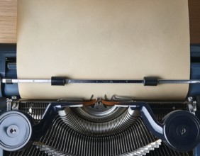 View from above of a retro typewriter equipped with a blank paper sheet, representing creativity,
