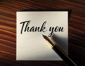 Elegant pen rests alongside a handwritten Thank You card on a wooden surface in soft light.
