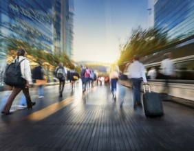 People with luggage walking on a modern city footbridge during sunset, showcasing urban life and