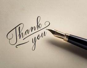 Elegant pen rests alongside a handwritten Thank You card on a wooden surface in soft light.