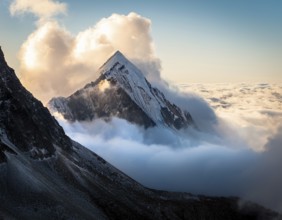 A stunning view of a snowy mountain peak rising above the clouds, with a blue sky background.