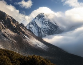 A stunning view of a snowy mountain peak rising above the clouds, with a blue sky background.
