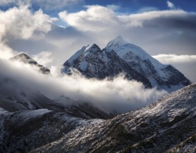 A stunning view of a snowy mountain peak rising above the clouds, with a blue sky background.