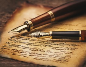 Close-up of a classic fountain pen lying atop old aged paper on a wooden surface, symbolizing