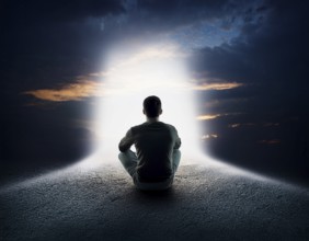 An individual sits in quiet contemplation near the ocean during sunset, surrounded by dramatic