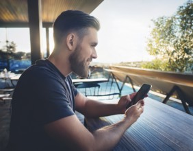 A person holding a smartphone at an outdoor cafe amidst a vibrant and lively urban setting. The