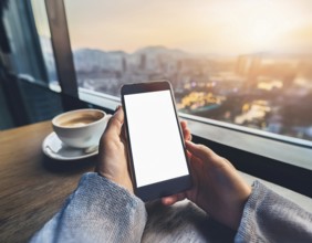 A person holding a smartphone at an outdoor cafe amidst a vibrant and lively urban setting. The