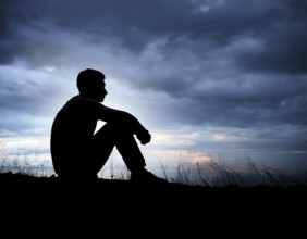 A silhouette of a person seated on the floor, conveying feelings of sadness and solitude against a