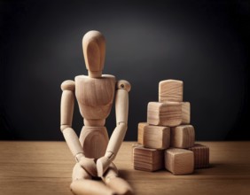 A wooden mannequin seated at a table conveys emotions of stress, thought, and contemplation.