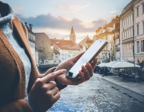 A person holding a smartphone at an outdoor cafe amidst a vibrant and lively urban setting. The