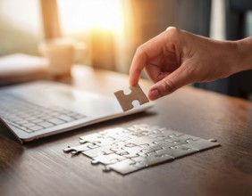 A person's hand placing a puzzle piece on a reflective surface in an office setting as the sun