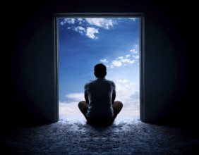 Silhouette of a person sitting alone within a brick archway, observing a peaceful and scenic cloudy