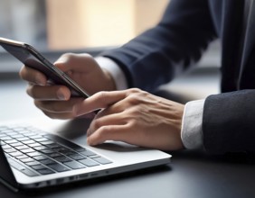 A man in a professional office environment multitasking with a smartphone and laptop, conveying