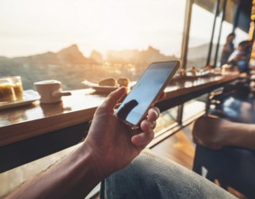 A person holding a smartphone at an outdoor cafe amidst a vibrant and lively urban setting. The