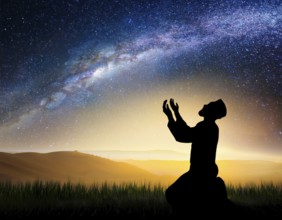 A man kneels in peaceful reflection under the vibrant Milky Way galaxy at sunset in an open natural