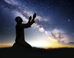 A man kneels in peaceful reflection under the vibrant Milky Way galaxy at sunset in an open natural