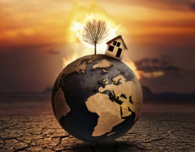 A miniature house and bare tree on cracked soil with a vivid orange sunset, symbolizing