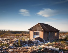 An abandoned house sits amidst scattered garbage in a deserted rural area, conveying environmental