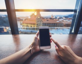 A person holding a smartphone at an outdoor cafe amidst a vibrant and lively urban setting. The