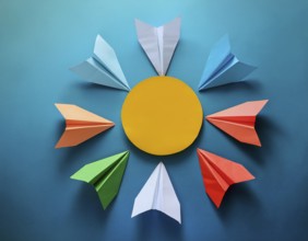Six colorful origami paper airplanes are displayed in a creative arrangement on a bright