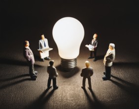 Miniature people standing around a glowing light bulb symbolizing creativity, teamwork, and