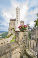 A tall tower with pink flowers in a stone wall arrangement in front of a castle, Lichtenstein