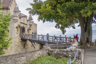 People crossing an old stone bridge towards a castle, surrounded by trees, Lichtenstein Castle,