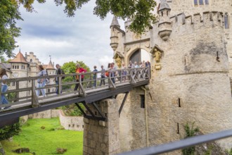 Group of tourists crossing a historic wooden bridge at a majestic castle gate, Lichtenstein Castle,