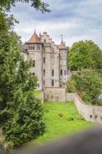 A castle surrounded by trees and stone walls, with a clear sky in the background, Lichtenstein