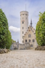 Majestic castle with towers and manicured hedges, captured from a view along a cobbled path,
