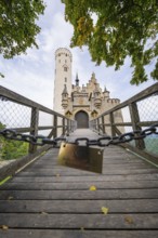 A bridge leads to a majestic Gothic-style castle surrounded by autumnal trees, Lichtenstein Castle,