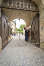 People pass a large wooden stone gate leading to a castle, Lichtenstein Castle, Lichtenstein,