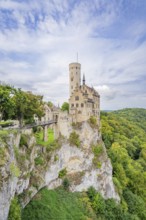 Medieval castle with high tower on a rocky outcrop surrounded by lush green forests and dramatic