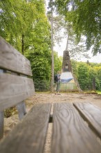 Woman with rucksack looking at a monument in the forest, near a wooden bench, Lichtenstein Castle,