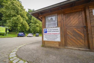 A small car park with a wooden hut and parked cars at the edge of the forest, Lichtenstein Castle,