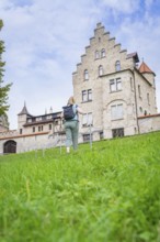 A woman walks up a grassy hill towards an imposing historic castle, Lichtenstein Castle,