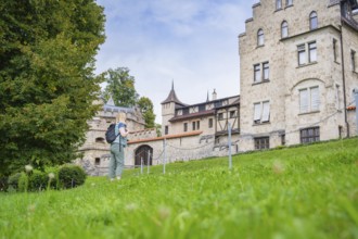 A woman next to a historic building with a green meadow and trees in the background, Lichtenstein