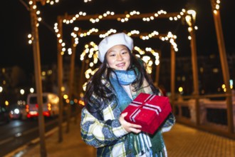 Smiling young woman holding christmas present enjoying winter holidays season under decorative
