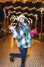 Happy young woman holding a christmas gift, reveling in the enchanting glow of festive lights and