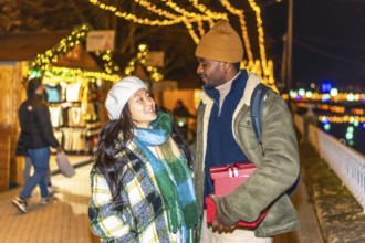 Happy multi ethnic couple enjoying christmas time together, exchanging gifts at a magical christmas