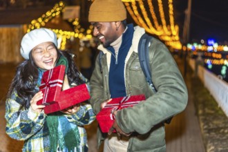 Young multiethnic couple exchanging christmas gifts at a christmas market, enjoying the festive