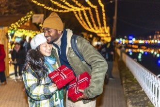 Multiethnic couple embracing and joyfully exchanging christmas gifts at a vibrant christmas market,