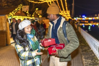 Happy multiethnic couple exchanging christmas gifts at a christmas market, enjoying winter holidays