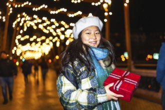 Young asian woman holding red christmas gift enjoying christmas lights decoration at night in the