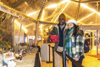 Multiethnic couple holding christmas gifts looking at a nativity scene in a christmas village