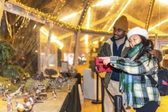 Happy multiethnic couple holding christmas gifts and enjoying a nativity scene exhibition