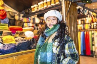 Young woman wearing a beret and scarf, smiling at a christmas market stall selling winter clothes